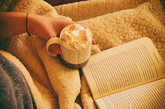 Reading in bed with a book and a cup of coffee in hand (stock photo)